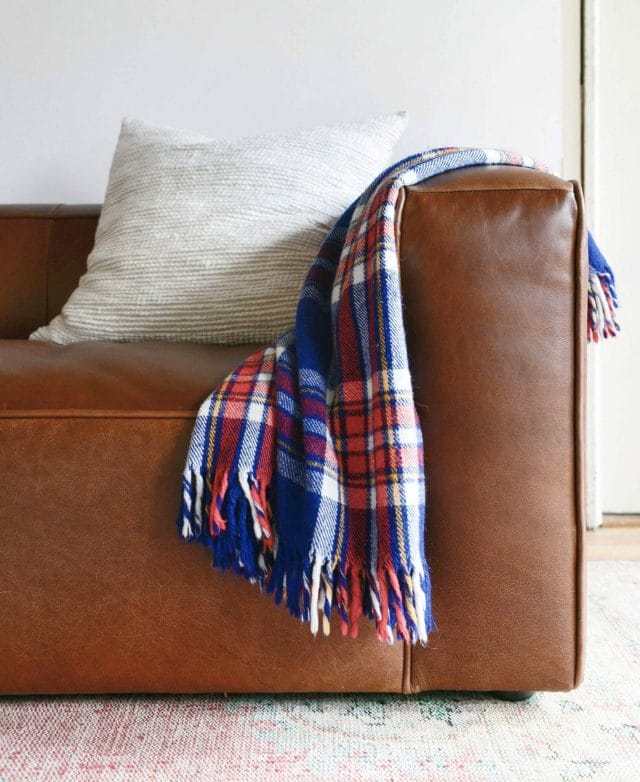 A plaid throw is draped over an Article leather sofa from Yellow Brick Home