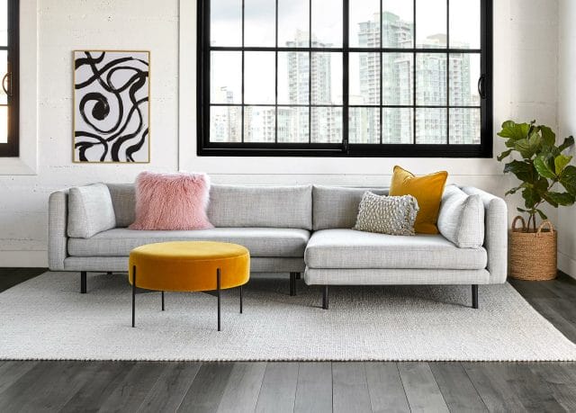 Article's Lappi Sectional in a light gray sits next to a yellow ottoman and black and white print.