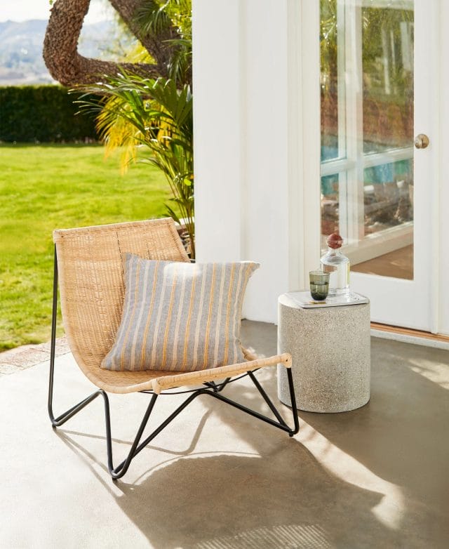 The rattan Ikast Lounge Chair is shown with an accent pillow and side table.