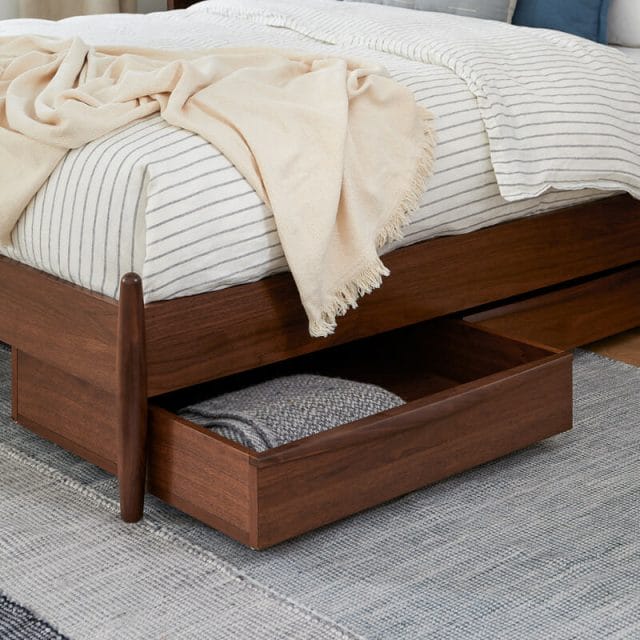 A brown oak drawer underneath a comfortable white bed. 