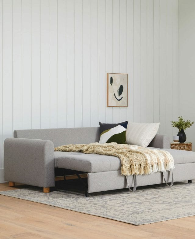 A comfy, gray sofa bed with a fluffy yellow throw blanket.