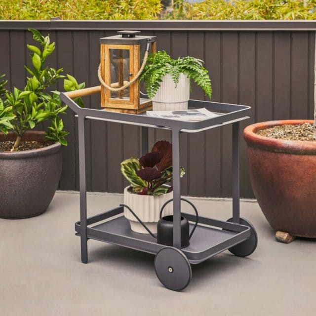 A gray bar cart holding plants and a lantern on an outdoor patio