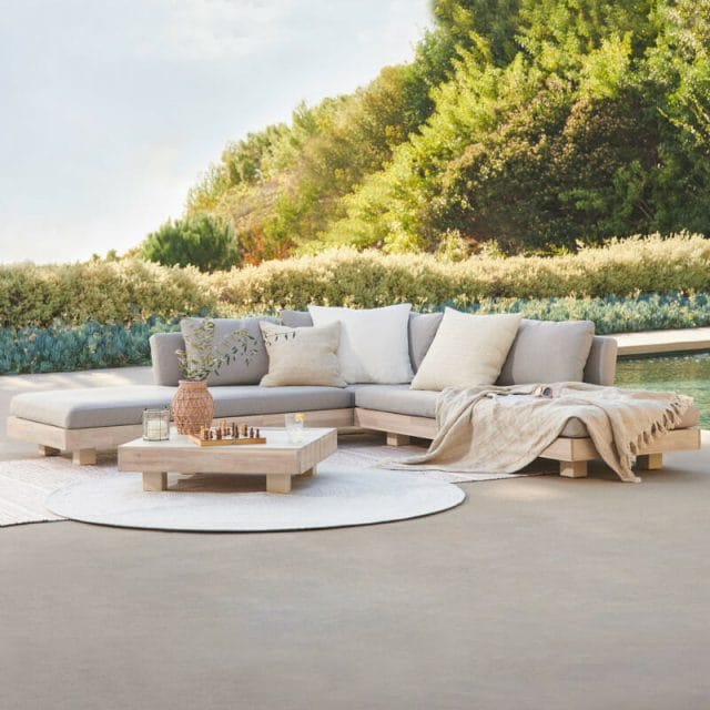 Gray outdoor sectional sofa on a white rug with a wood coffee table.